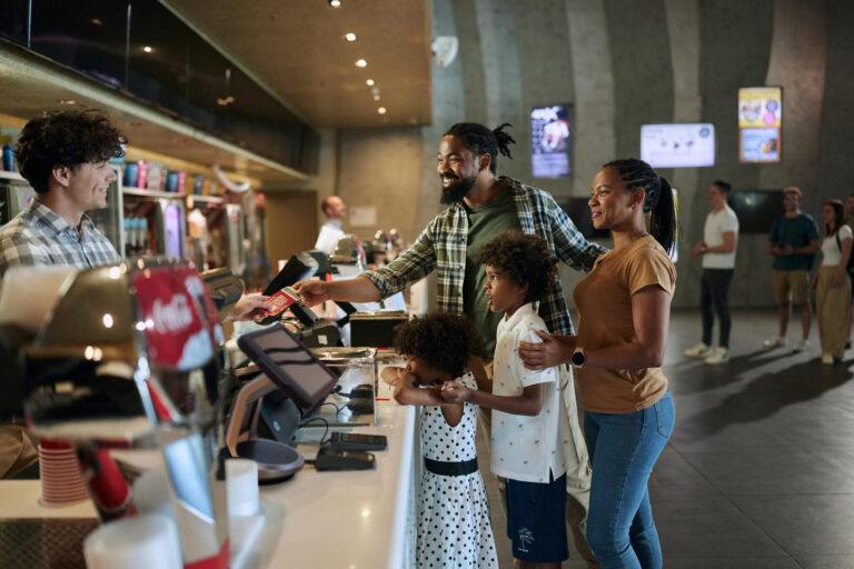 Genitori afroamericani felici e i loro figli acquistano biglietti presso il chiosco dell'arena dedicata agli articoli sportivi.