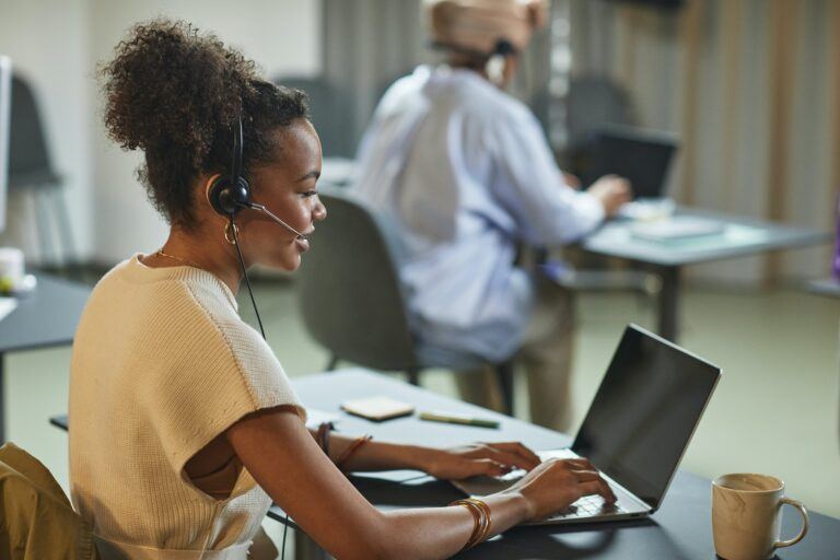 Donna seduta davanti a un computer portatile con cuffie per il servizio clienti