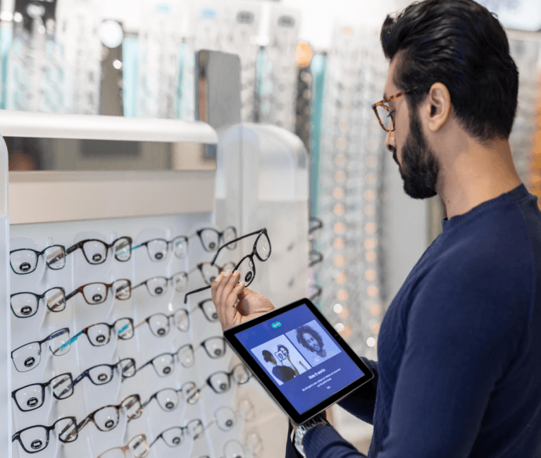 Uomo che tiene in mano un paio di occhiali mentre impugna un tablet