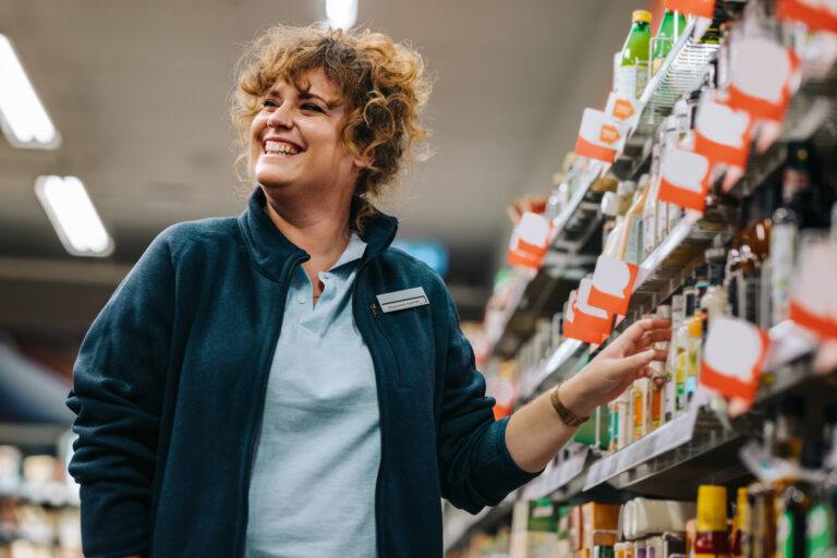 Donna d'affari sicura di sé in piedi davanti agli scaffali e sorridente in un supermercato. Direttrice di un negozio di alimentari.